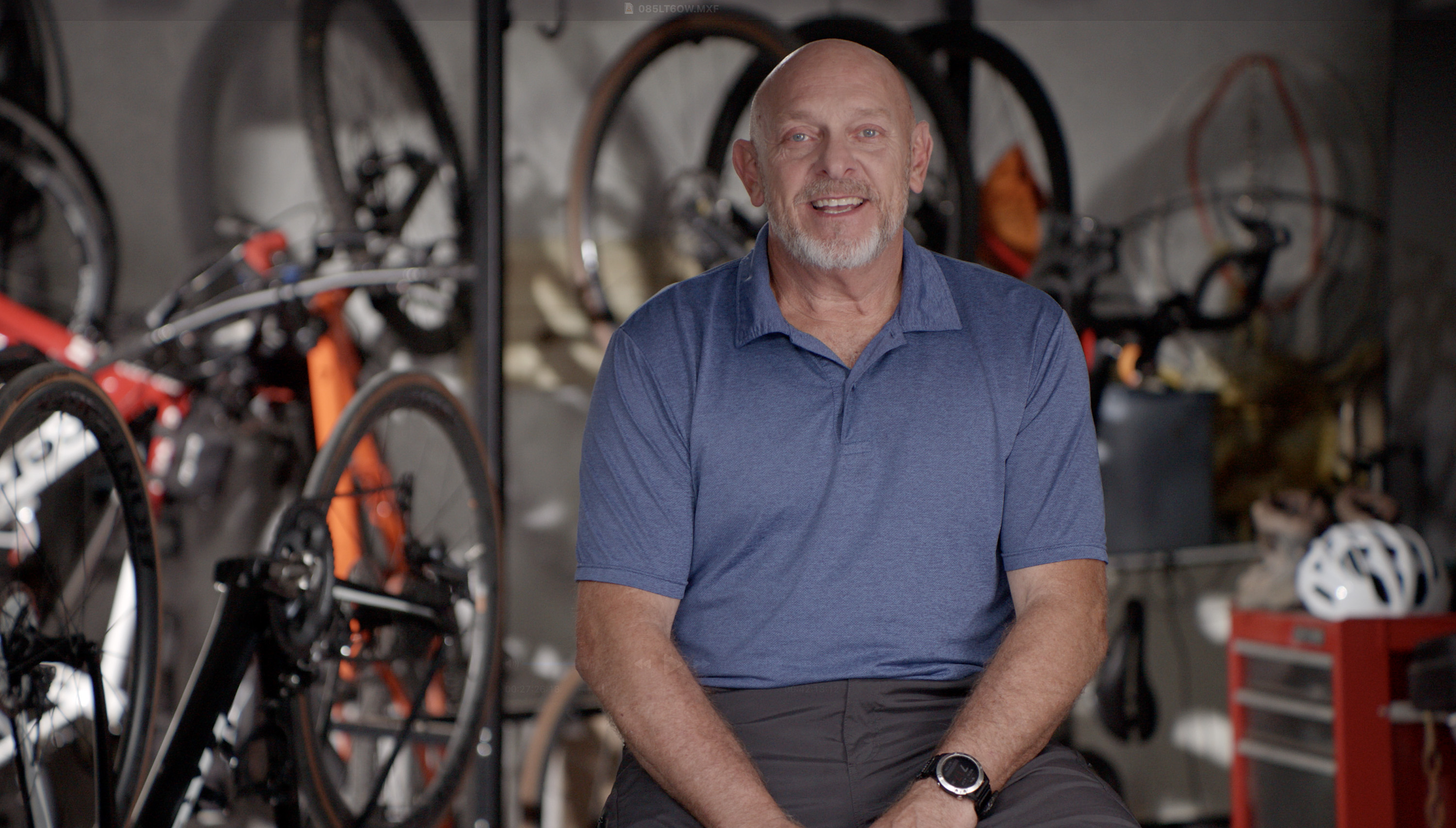 Man in blue shirt with bicycles hanging in background