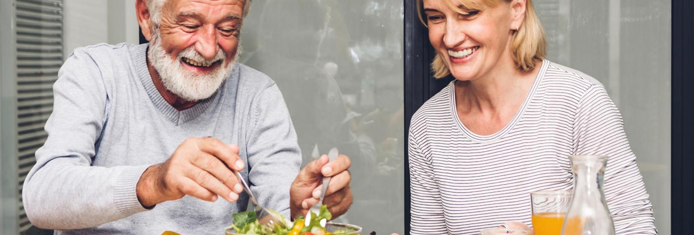 Older man and women eat a healthy meal at a dining table 