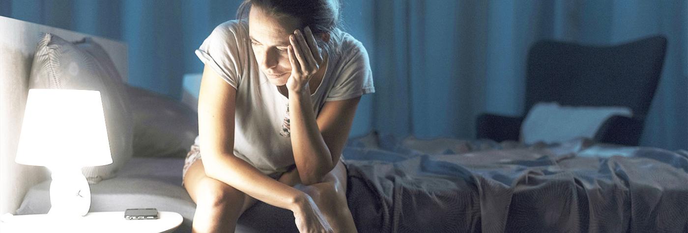 Woman sitting up on side of bed looking tired